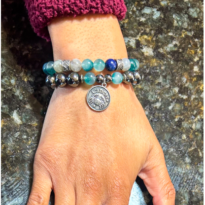 Hand wearing a double Cancer zodiac bracelet set with Hematite, Amazonite, Moonstone, and Sodalite beads, photographed on a granite surface.